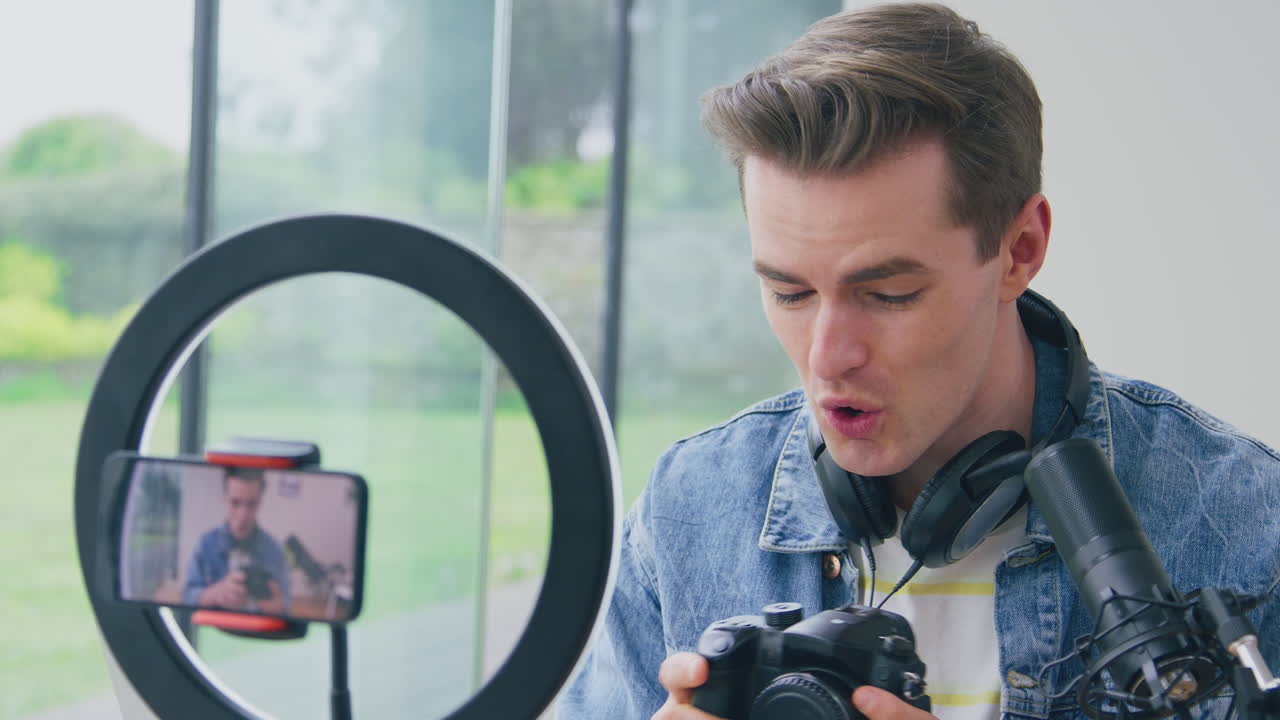 Vlogger uomo in diretta streaming recensisce una fotocamera a casa, video registrato con telefono cellulare.