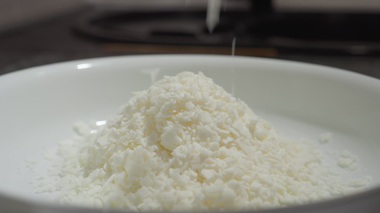 Close up of white flakes resembling baking powder being sprinkled into flat white plate on baking table in kitchen during ingredient preparation for baking with warm lighting and soft texture