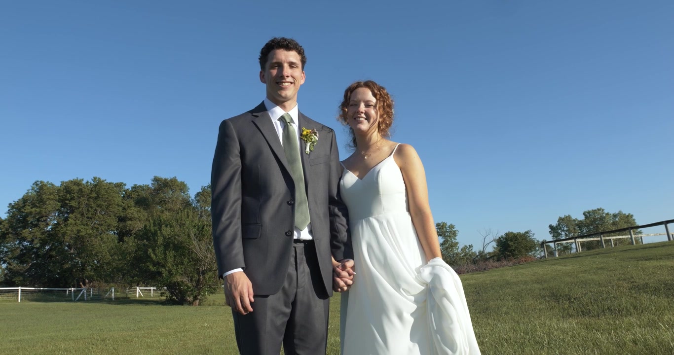Um casal de noivos alegre ri e dá as mãos enquanto caminha por um campo ensolarado, irradiando felicidade e amor no dia do casamento em meio a um belo cenário natural