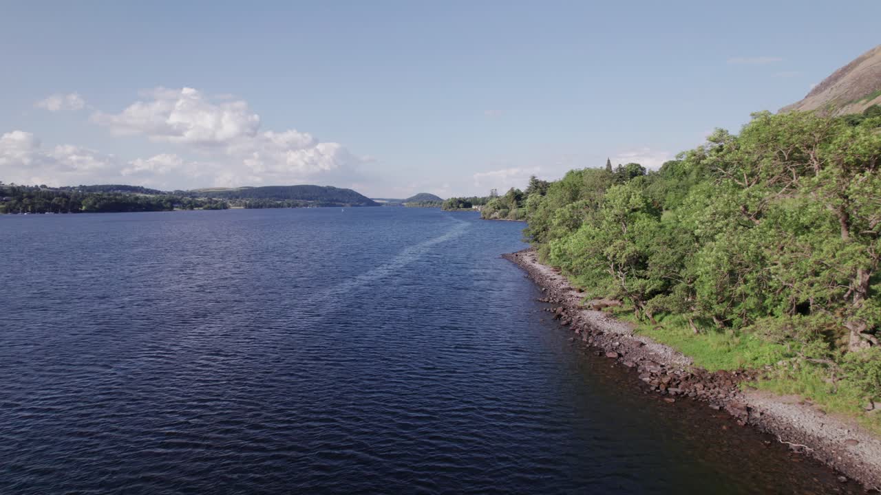 화창한 날, 울스워터, 호수 지구, 컴브리아, 영국에 호수 해안선을 따라 뒤로 날아가는 낮은 드론 샷