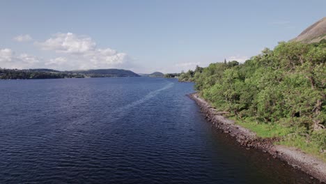 low drone shot flying backward along a lake shoreline on a sunny day, ullswater, lake district, cumbria, uk