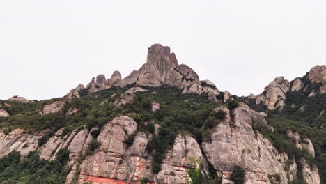 drone crane-down shot gracefully revealing the round cliff peaks of montserrat against the backdrop of a tranquil overcast day