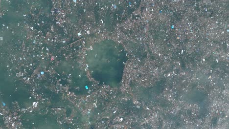 de arriba hacia abajo rápidamente ascendiendo drone tiro de agua contaminada llena de basura flotando sobre arrecife de coral muerto en el agua tropical turquesa de bali indonesia
