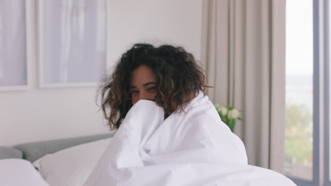 donna felice che gioca a letto che si diverte sotto le lenzuola che si gode una mattina spensierata a casa