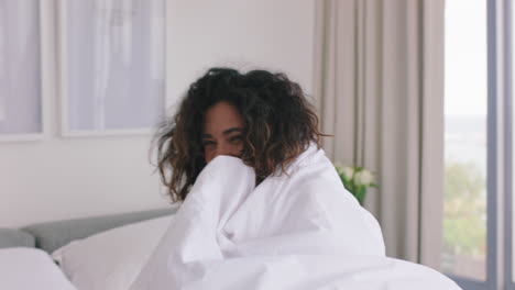 happy woman playing in bed having fun under sheets enjoying carefree morning at home