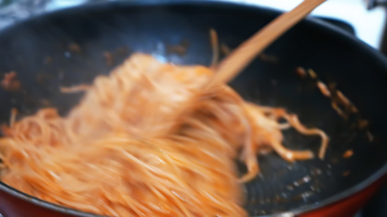 A man is stirring spaghetti with sausage in a pan on a stove