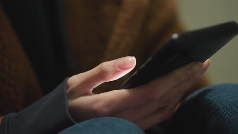 primer plano de una mano con un abrigo marrón y vaqueros azules, sosteniendo y desplazando un teléfono inteligente, los dedos interactuando con el dispositivo, capturando un momento de contemplación tranquila