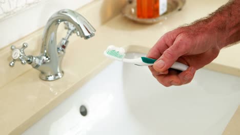 un homme âgé met du dentifrice sur une brosse à dents dans la salle de bain