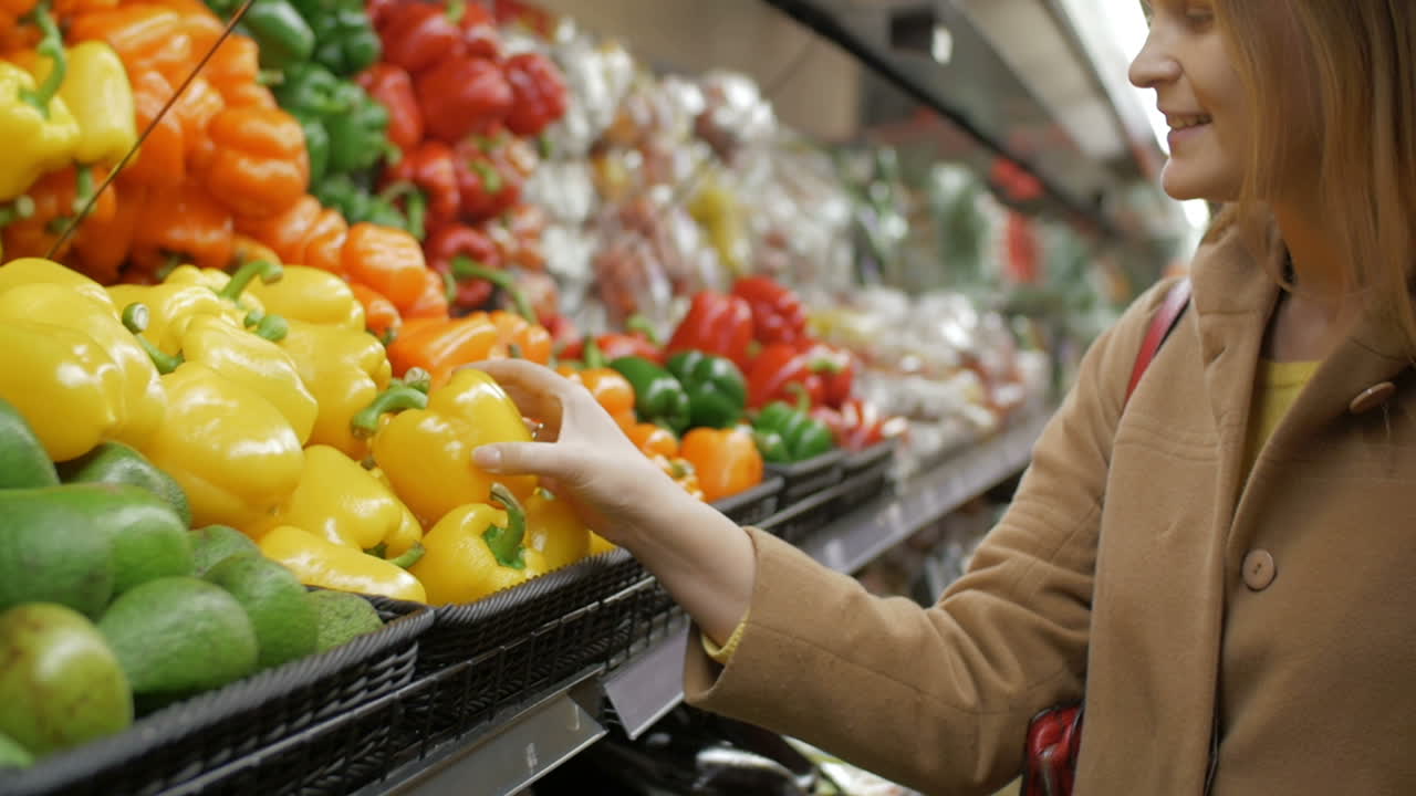 chica feliz comprando pimientos amarillos frescos en el supermercado