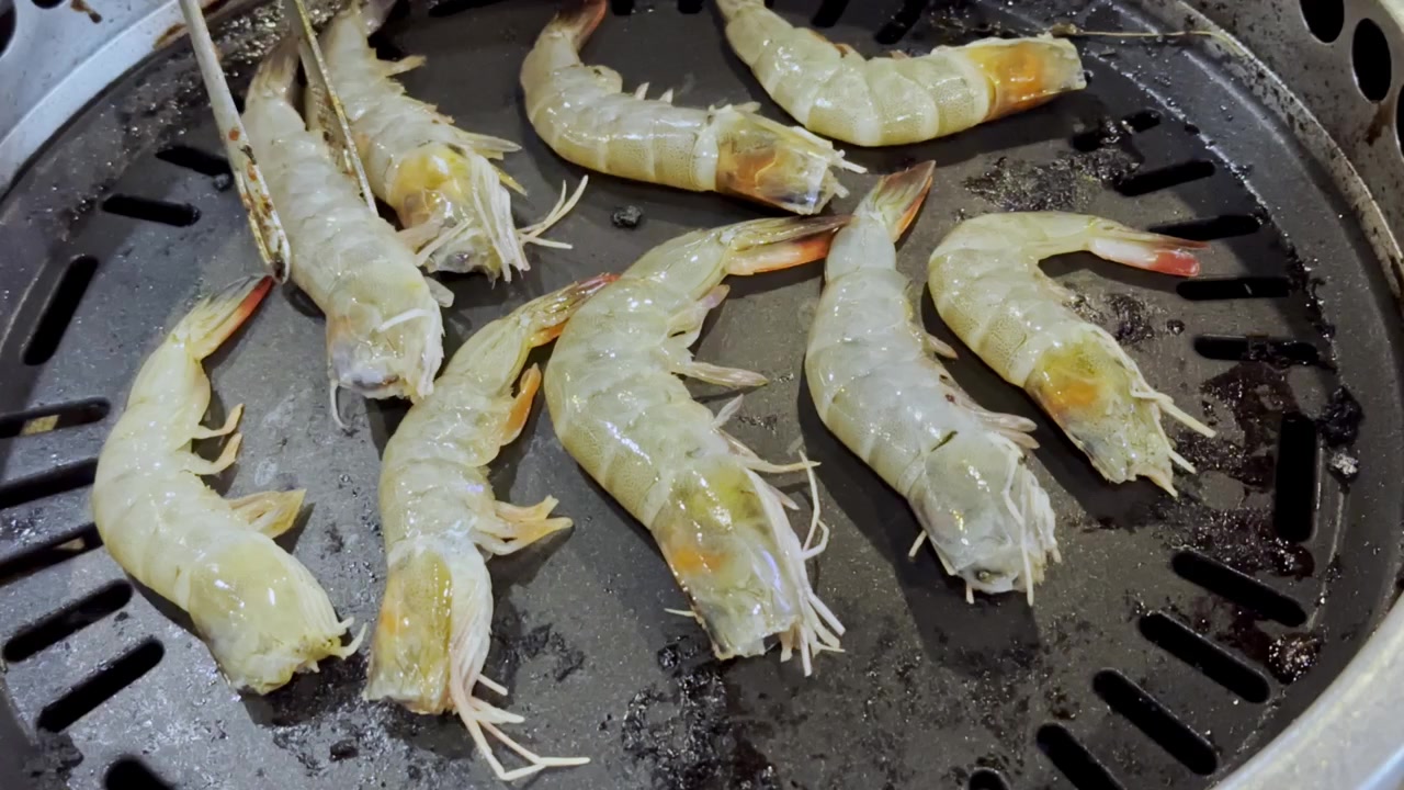 Primo piano di gamberi freschi che sfrigolano su una padella calda da barbecue, catturando frutti di mare succosi, vapore che sale e deliziosi sapori grigliati in una scena di cucina.