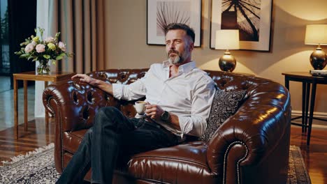 man relaxing on leather couch with coffee