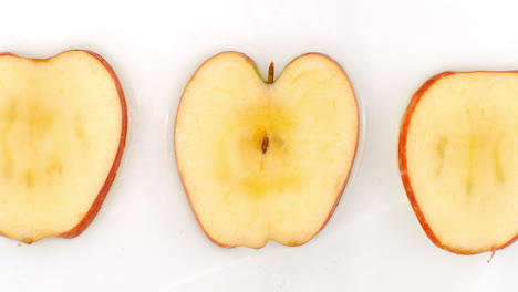 3 manzanas se encuentran en un blanco en el fondo en cámara lenta cayendo salpicaduras de agua.