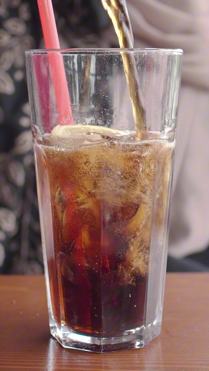Versare cola in un bicchiere con ghiaccio e fette di limone