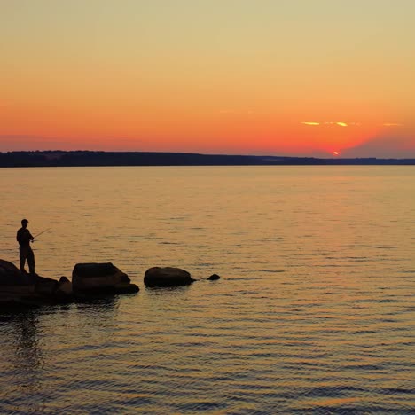 fisherman at the evening river. silhouette of a man fishing on the stone in water on the beautiful nature background at sunset.