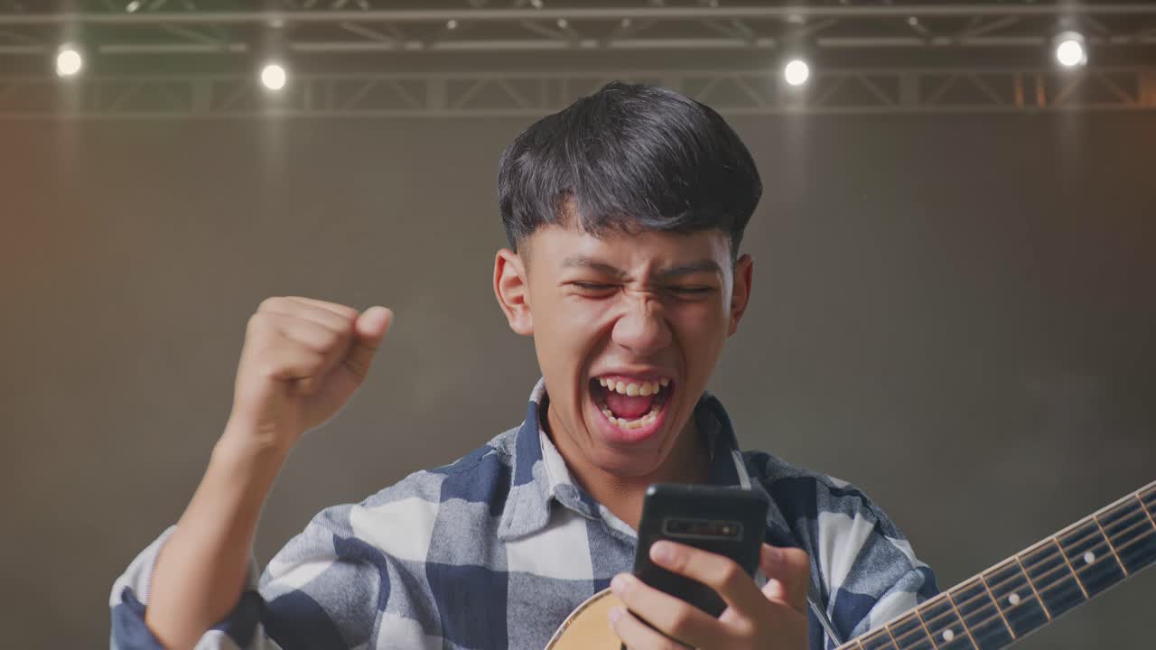 스마트폰을 이용해 기타를 들고 무대 위에 서서 성공을 축하하는 아시아 십대의 클로즈업