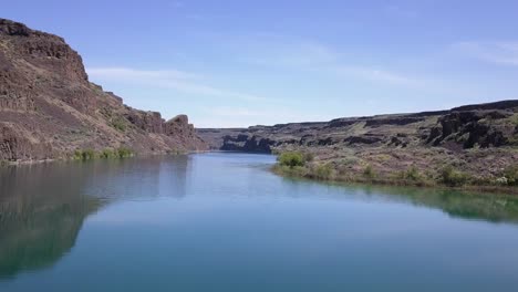 low pov skims along surface of deep blue lake in rugged, arid terrain