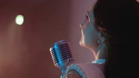 close-up view of a singer in a white gown performing with a vintage microphone. her hair flicks gently while she sings against a soft pink background