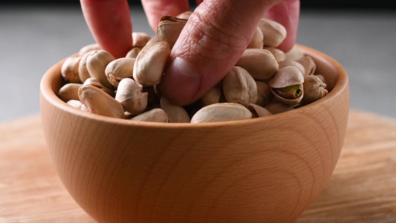 Primo piano di una mano che prende pistacchi da una ciotola di legno