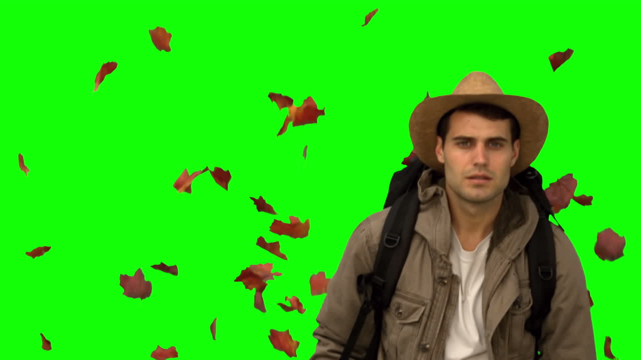 Uomo con un cappello che cammina sotto foglie che cadono su schermo verde