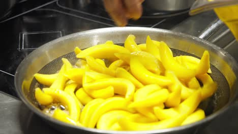 slow motion close-up of chef adding sliced yellow fruits to hot saucepan