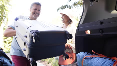 Feliz-Y-Diversa-Pareja-De-Ancianos-Empacando-Equipaje-En-Un-Auto-Al-Aire-Libre-Soleado