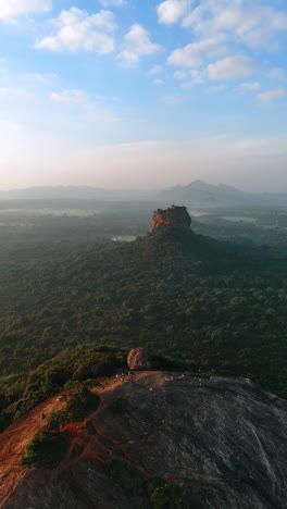 rock with almost no vegetation on. tourists walk by the mountain watching amazing sunset. aerial view of sri lanka. vertical video.