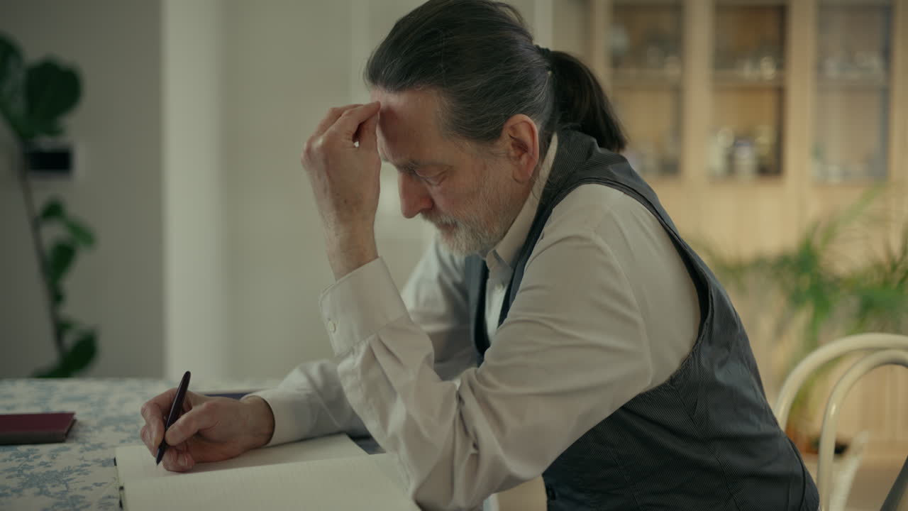 Uomo maturo pensieroso che si concentra mentre scrive a un tavolo.