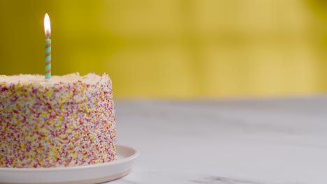 studio shot birthday cake covered with decorations and single candle being blown out 3