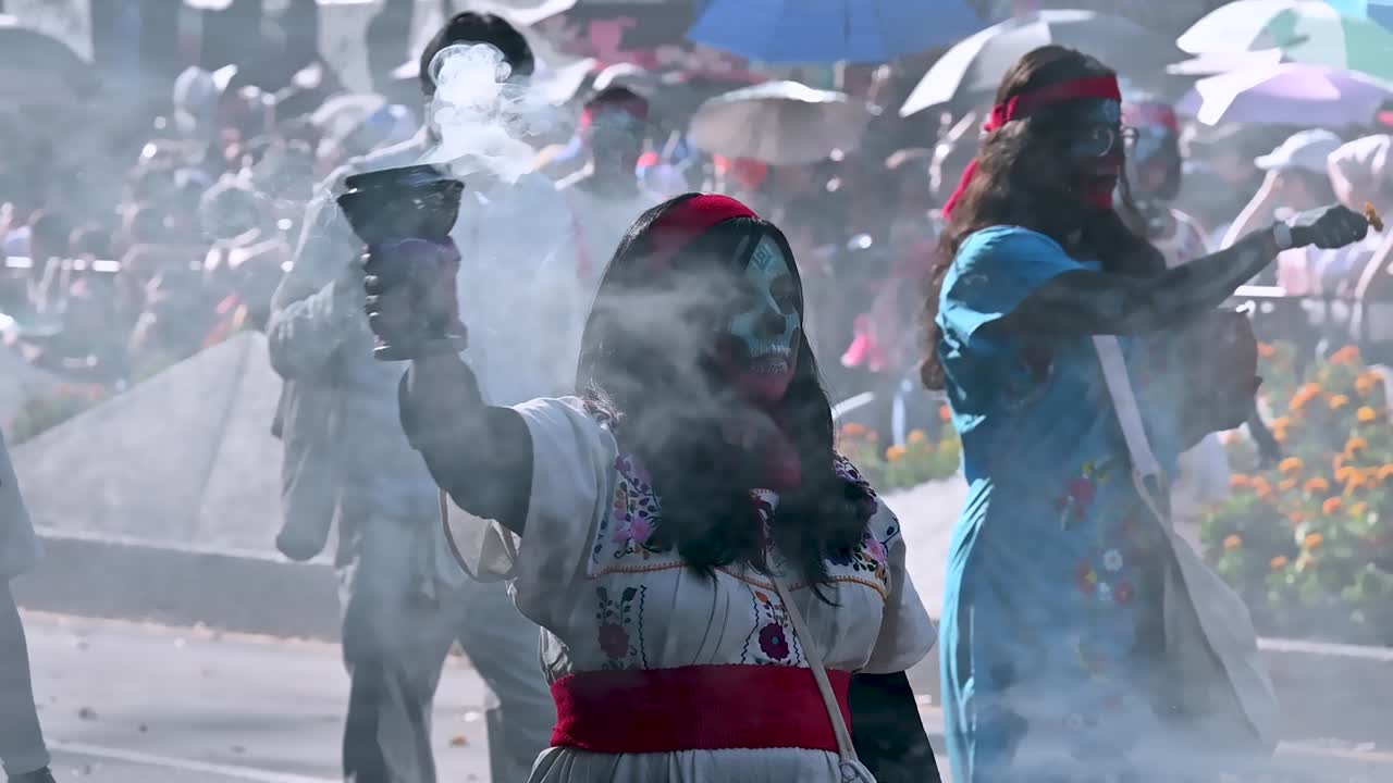 Performers in face paint and traditional costumes at the Day of the Dead parade in Mexico smoking urn filling air with grey cloud