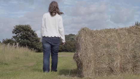 Woman-walking-in-field-with-bale-of-hay-wide-shot