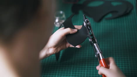 experienced tailor makes holes in black leather cat mask ear