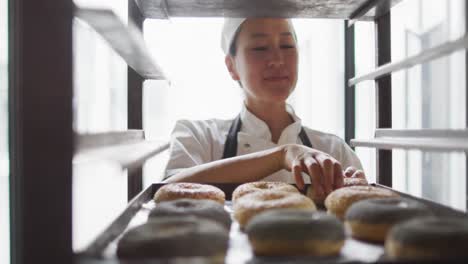 Animation-of-happy-asian-female-baker-checking-freshly-prepared-doughnuts