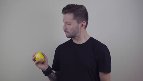 slow motion footage of a man with tattoos throwing a yellow apple in the air and catching it after