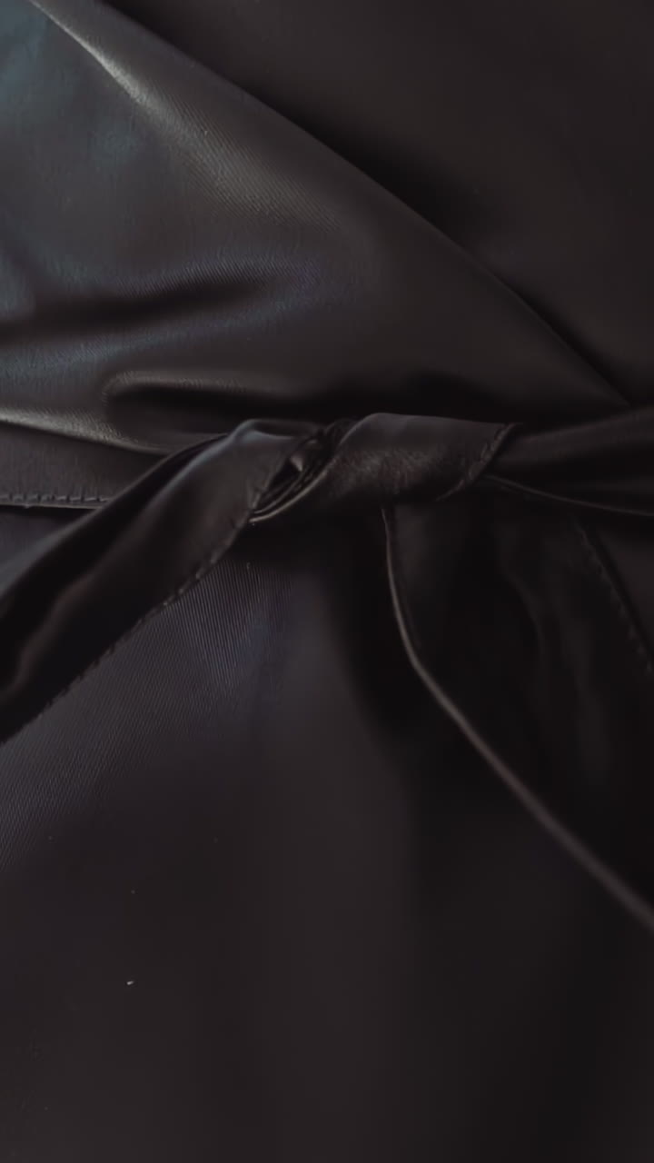 Woman unties long belt of elegant leather coat on dark background extreme close view slow motion. Stylish clothes design for everyday. Casual apparel