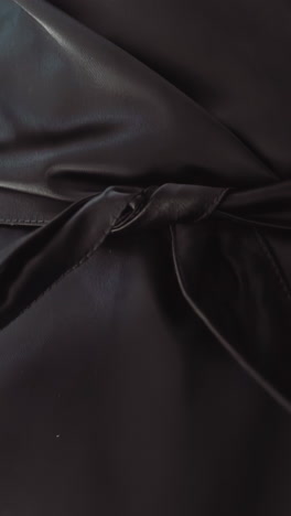 woman unties long belt of elegant leather coat on dark background extreme close view slow motion. stylish clothes design for everyday. casual apparel