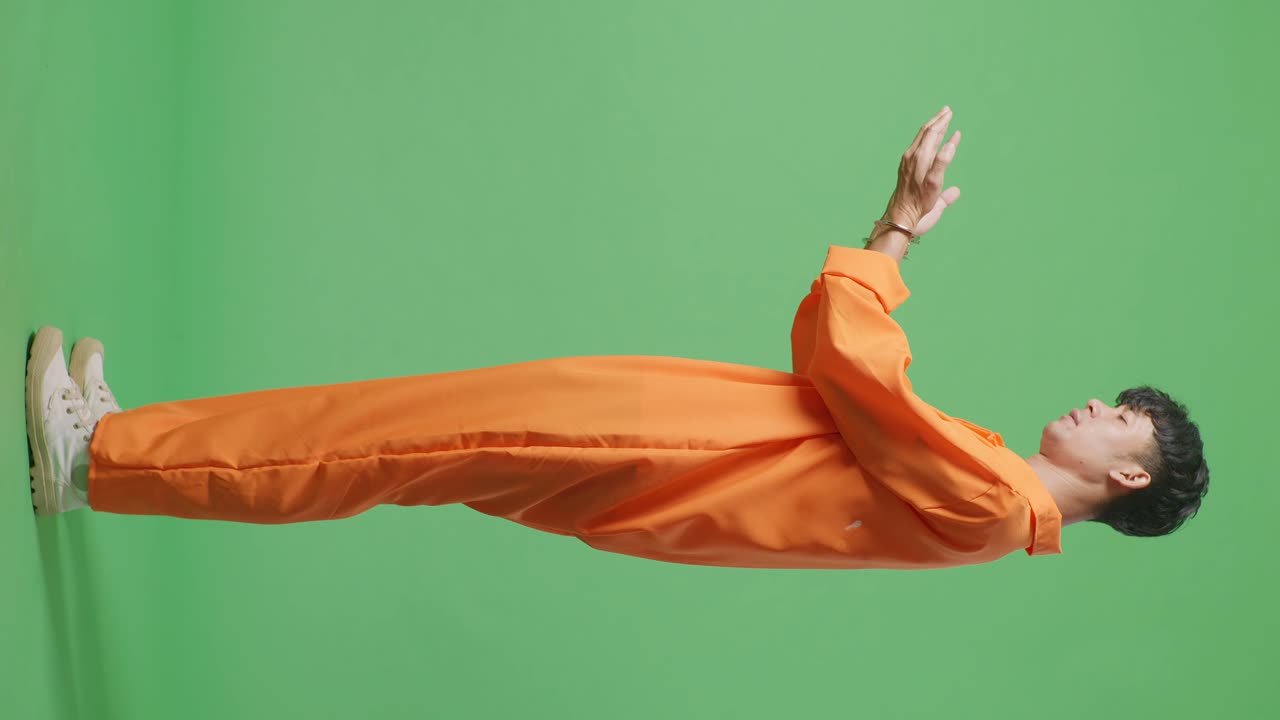 녹색 스크린 배경에 서있는 아시아 남성 수감자의 몸 전체 측면 뷰, 수갑을보고 그가 한 일에 화를 내며 머리를 흔들고 있습니다.