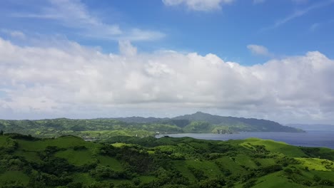 green hills by the ocean below thick clouds in batanes, philippines - high view