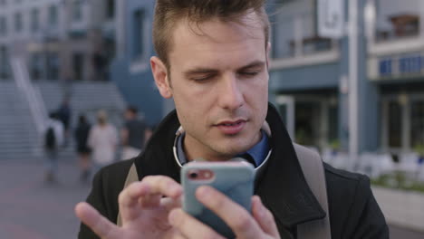 close up portrait of handsome young caucasian texting browsing using smartphone app in busy urban city