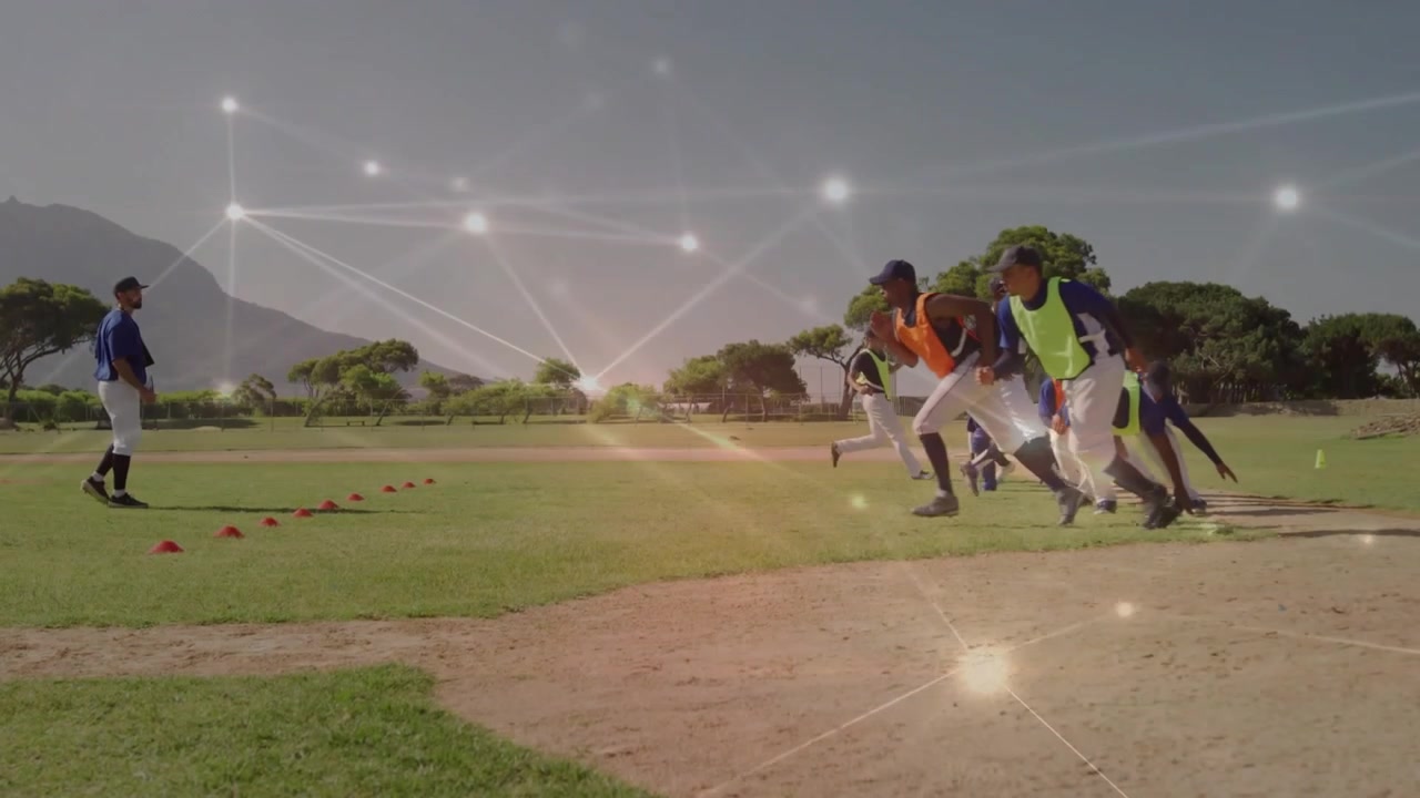 Entrenador asintiendo mientras los jugadores corren a toda velocidad desde el césped, pasando los conos, hacia la tierra durante un ejercicio de velocidad de béisbol.