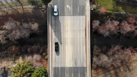 Aerial-footage-looking-down-and-pulling-back-on-bridge-road-over-creek-with-cars-passing