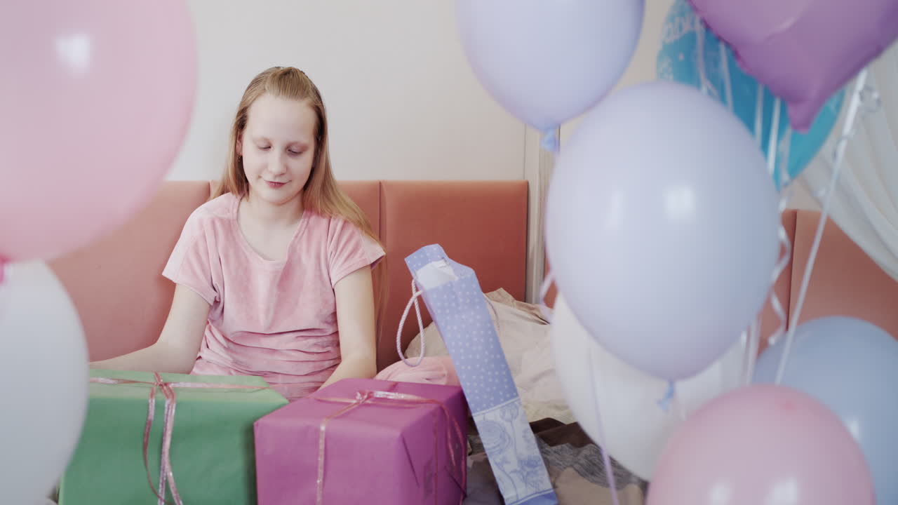 la niña recibió muchos regalos de cumpleaños, se sienta en la cama cerca de hermosas cajas, al lado de los globos