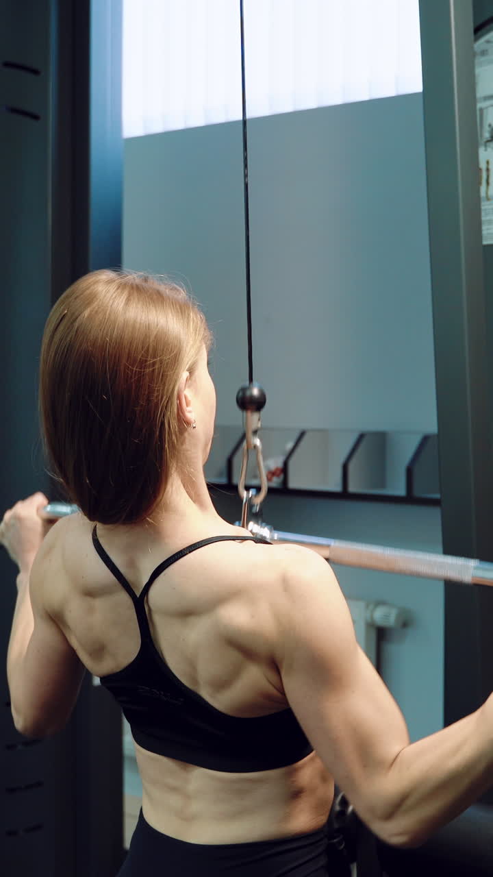A strong woman in black top is doing vertical traction in the training in the fitness club. Close-up Vertical video