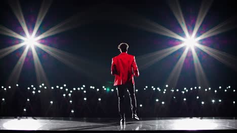 charismatic singer wearing vibrant red jacket performing with high energy, commanding stage through dynamic interaction, illuminated by bright spotlights and fans' mobile phone lights