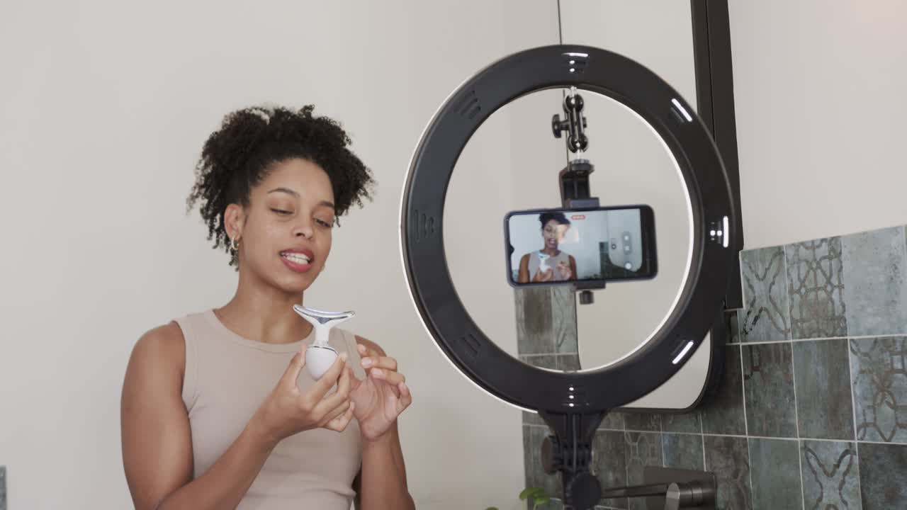 African American woman filming skincare demo with ring light, rotating handheld device to demo