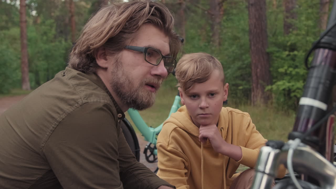 Father And Son Repairing Bike Outdoors In Forest
