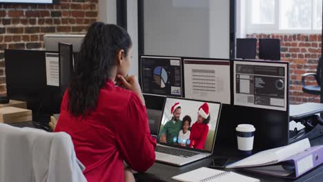 mujer de raza mixta usando computadora portátil en video chat en navidad en la oficina