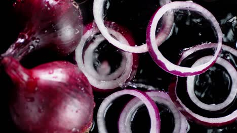 on whole and rings of red onion falling water drops.