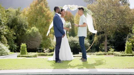 biracial man officiating marriage of happy african american couple in sunny garden, in slow motion