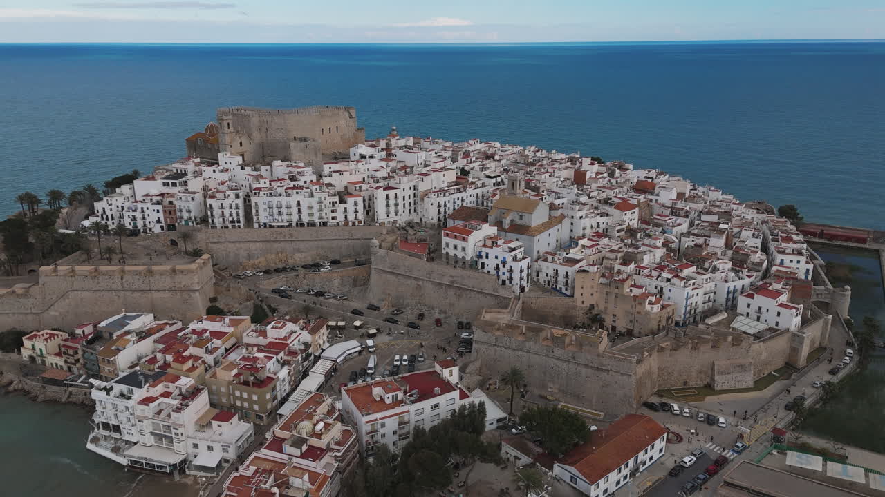 Drone establishing over Peniscola coastline and castle buildings above rocky beach terrain
