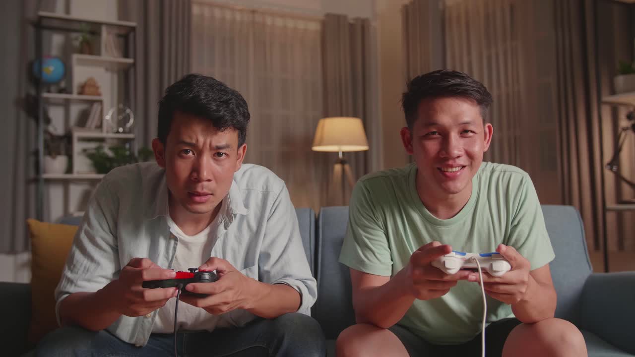 Asian Friends Playing Video Games At Home. Male Happy To Win Victory And Another Man Feeling Disappointed